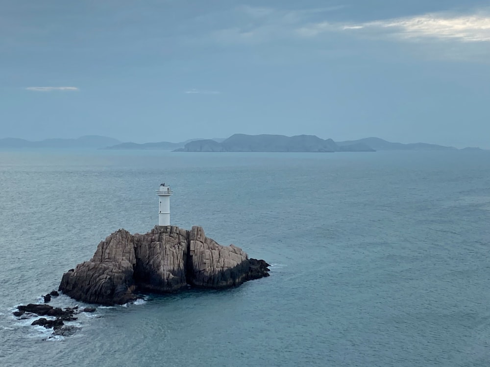 Phare blanc sur une formation rocheuse brune au milieu de la mer pendant la journée