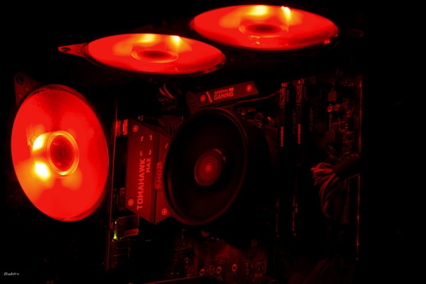 A sleek gaming-style desktop motherboard with illuminated NVMe SSD and DDR5 RAM installed, glowing in electric blue against a charcoal grey background.