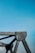A close-up view of a metallic structural component with rivets against a clear blue sky. The structure has angular lines and industrial design, suggesting part of a bridge or architectural framework.