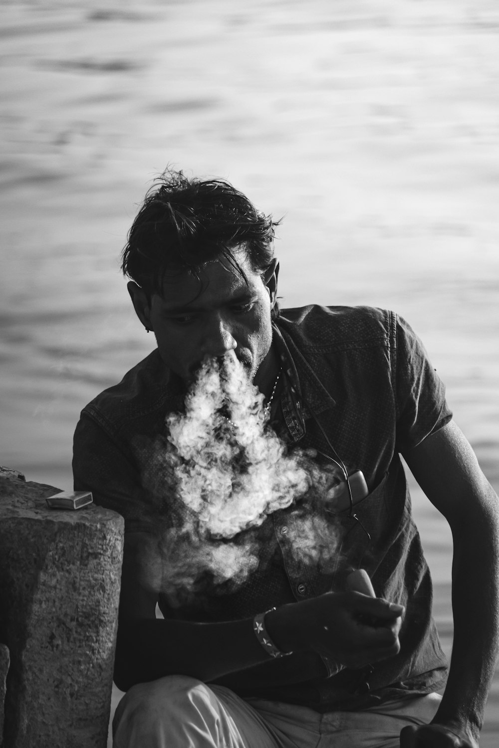Foto en escala de grises de un hombre con camiseta negra fumando un cigarrillo