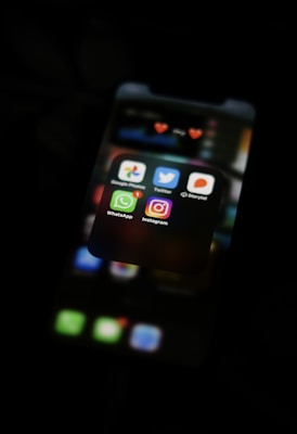 A smartphone screen displays several social media and communication app icons, including Google Photos, Twitter, Storytel, WhatsApp, and Instagram, with a notification badge on WhatsApp. The screen is dimly lit, set against a dark background.