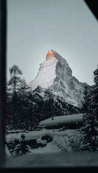 Snow-capped mountain peaks with a stylish cabin emitting warm light at dusk.