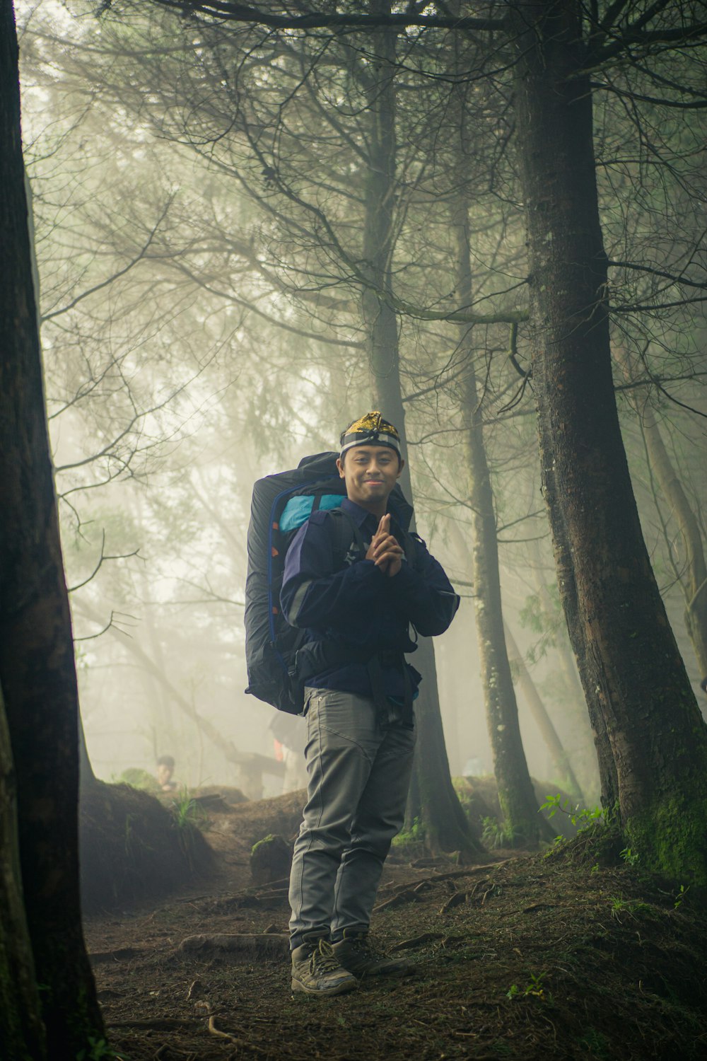 man in black jacket and brown pants wearing black backpack standing in forest during daytime