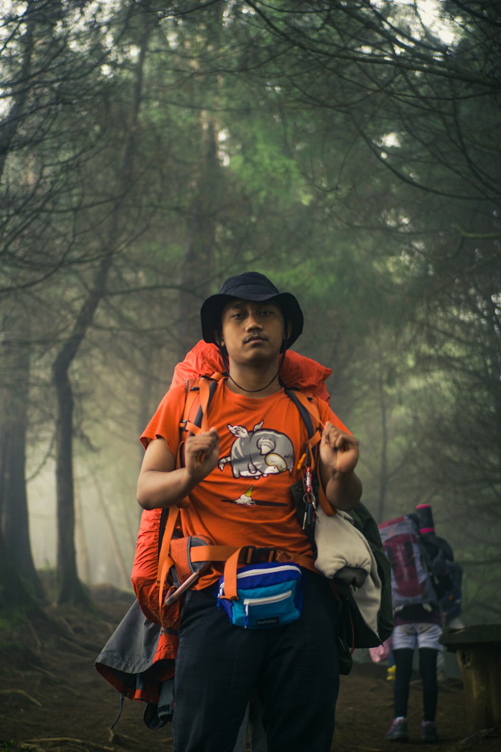 man in orange t-shirt and black hat carrying backpack