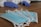 Several blue disposable face masks are laid out on a wooden surface. A pair of hands wearing blue gloves can be seen in the background.