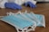 Several blue disposable face masks are laid out on a wooden surface. A pair of hands wearing blue gloves can be seen in the background.