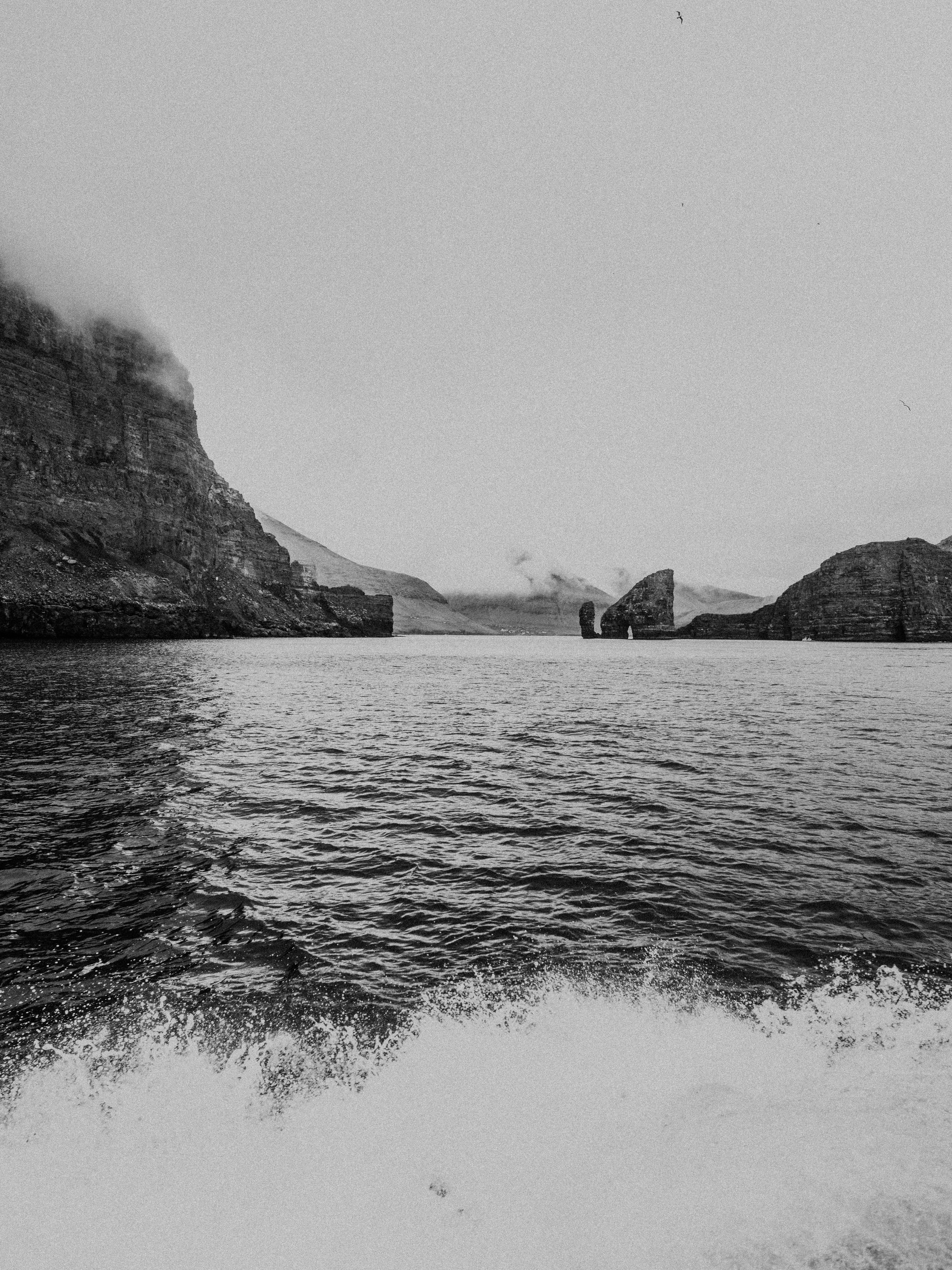 grayscale photo of body of water near mountain
