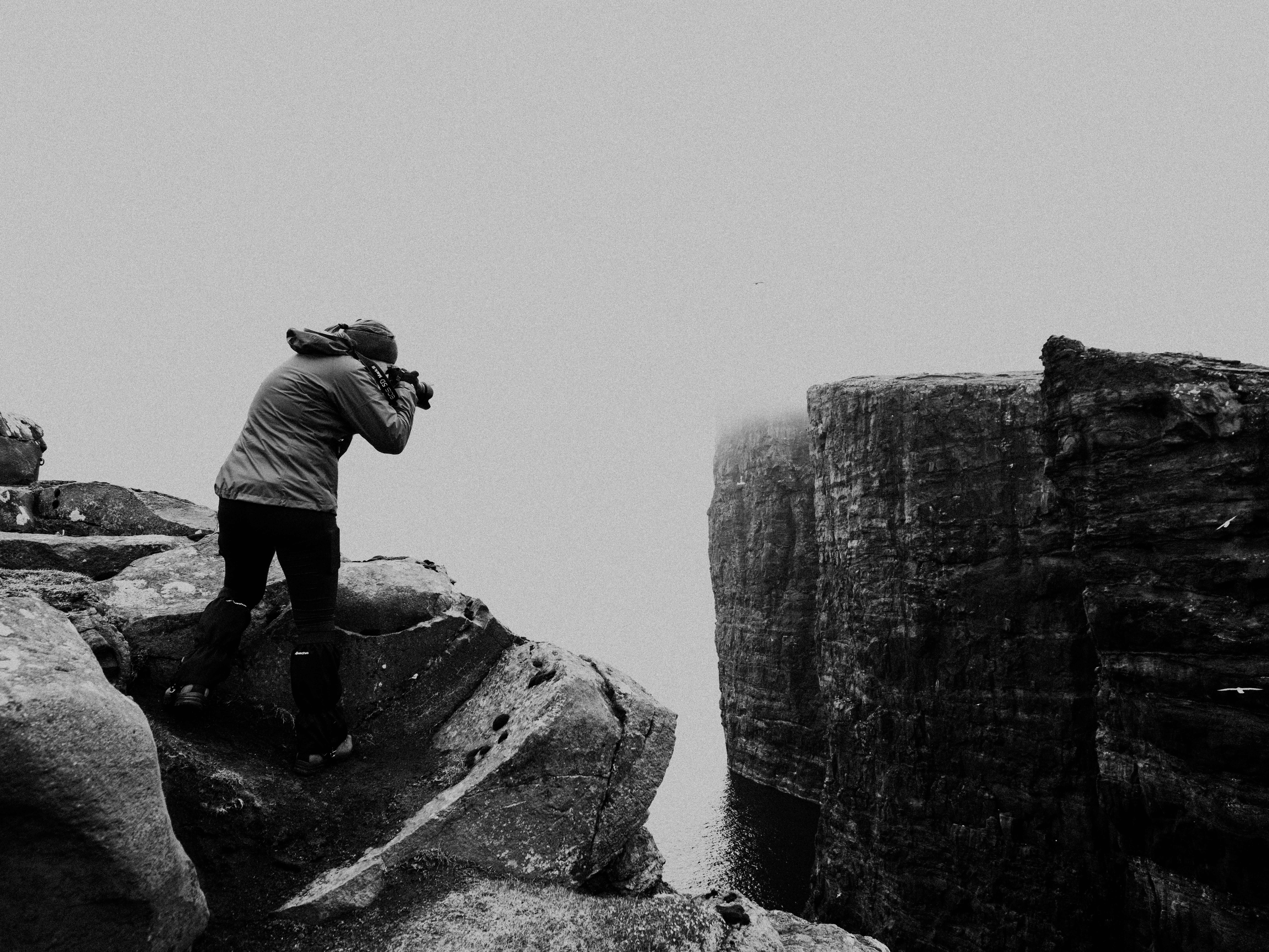 man in black pants and white long sleeve shirt standing on rock formation