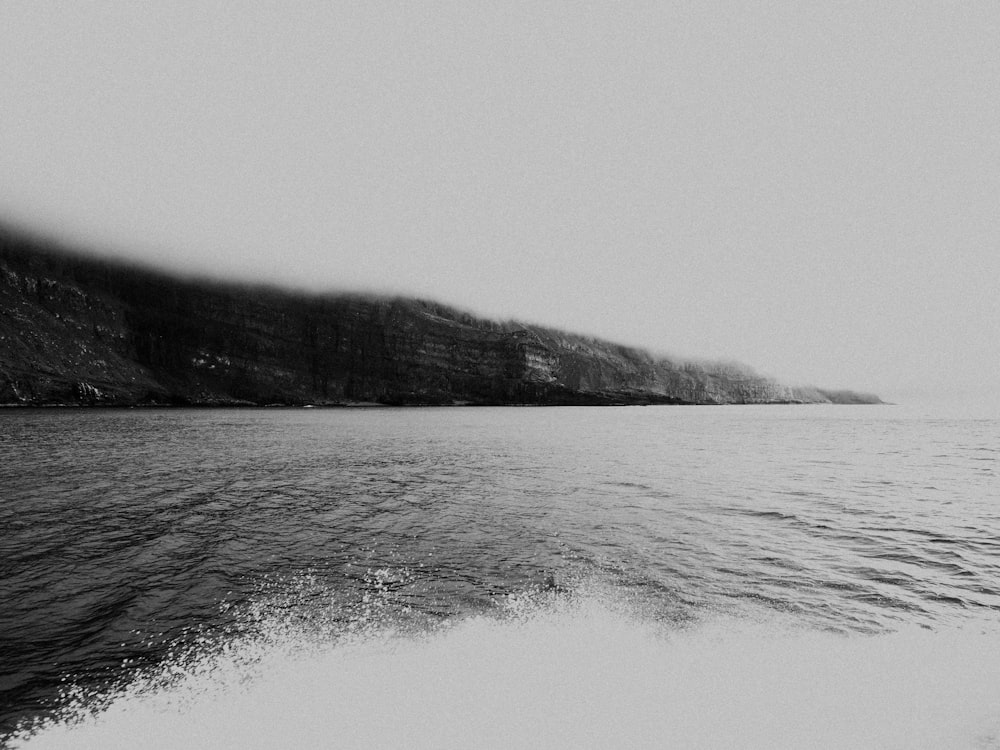 grayscale photo of ocean near mountain