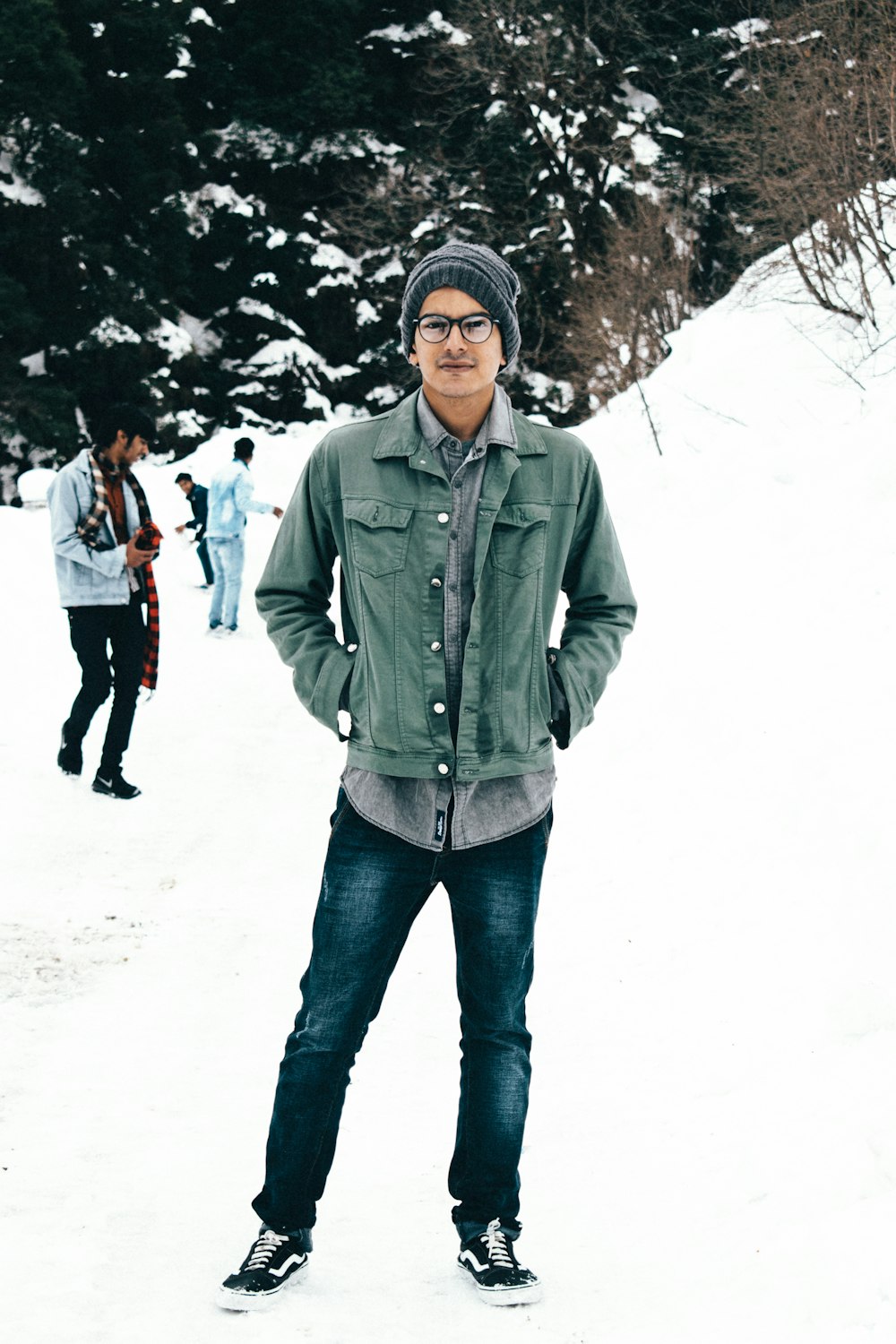 man in green zip up jacket and blue denim jeans standing on snow covered ground during