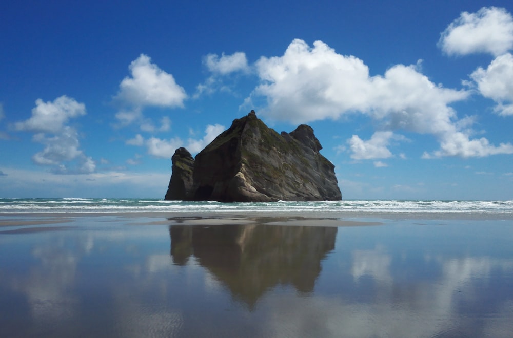 brown rock formation on sea shore under blue sky and white clouds during daytime