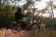 A motorcyclist wearing Veloire gloves and jacket, riding through a winding forest road at sunset.