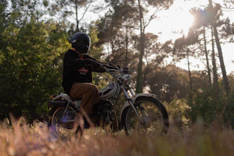 A motorcyclist wearing Veloire gloves and jacket, riding through a winding forest road at sunset.