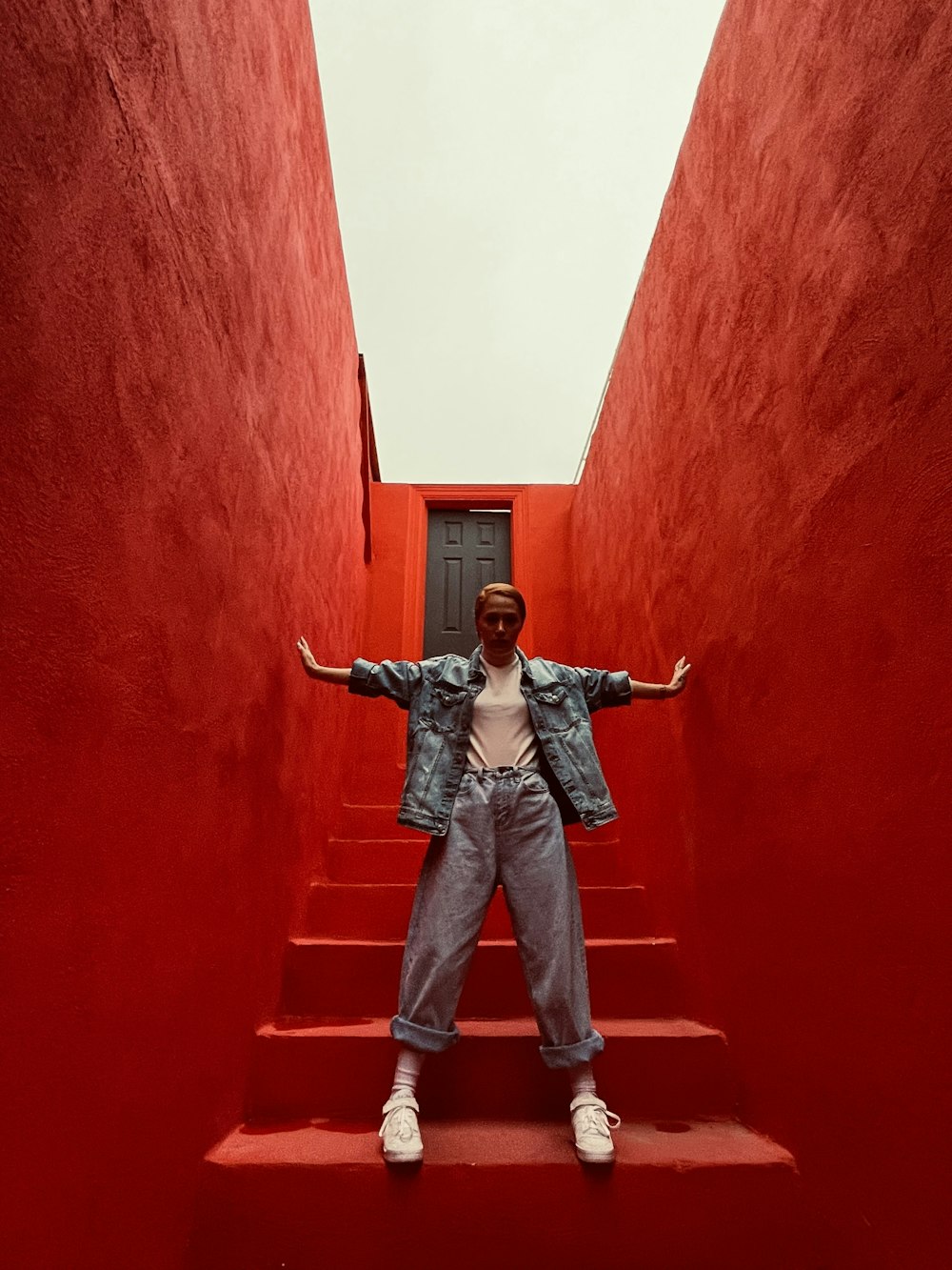赤いコンクリートの壁に立つ黒いジャケットとブルーデニムジーンズの男