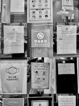 A collage of various signs and posters related to COVID-19 safety measures, displayed in what appears to be a public space. The signs include instructions for mask-wearing, social distancing, sanitation, and operational notices for businesses. Several signs also emphasize cleanliness and safety in environments like coffee shops, with images of masks, hand washing, and social distancing icons.