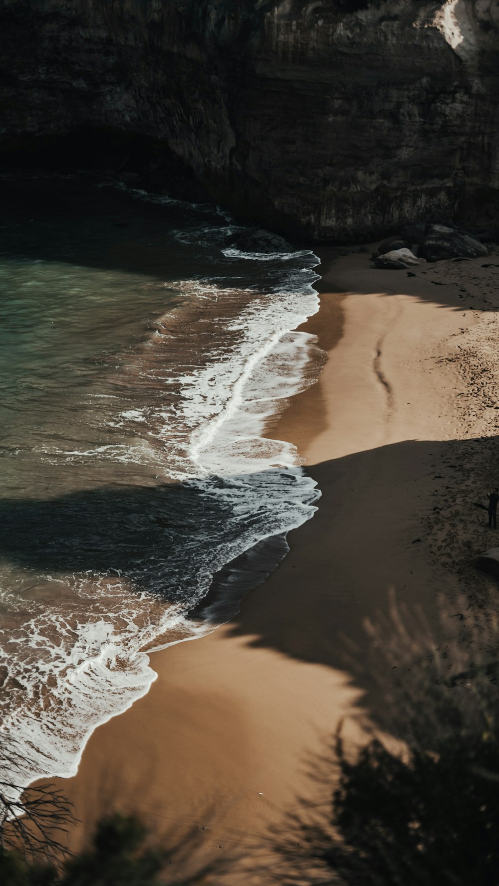 Plage de sable brun avec des vagues d’eau s’écrasant sur le rivage pendant la journée