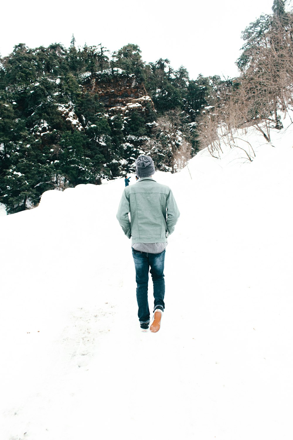 グレーのジャケットとブルーデニムのジーンズを着た男性が、昼間、雪に覆われた地面に立つ