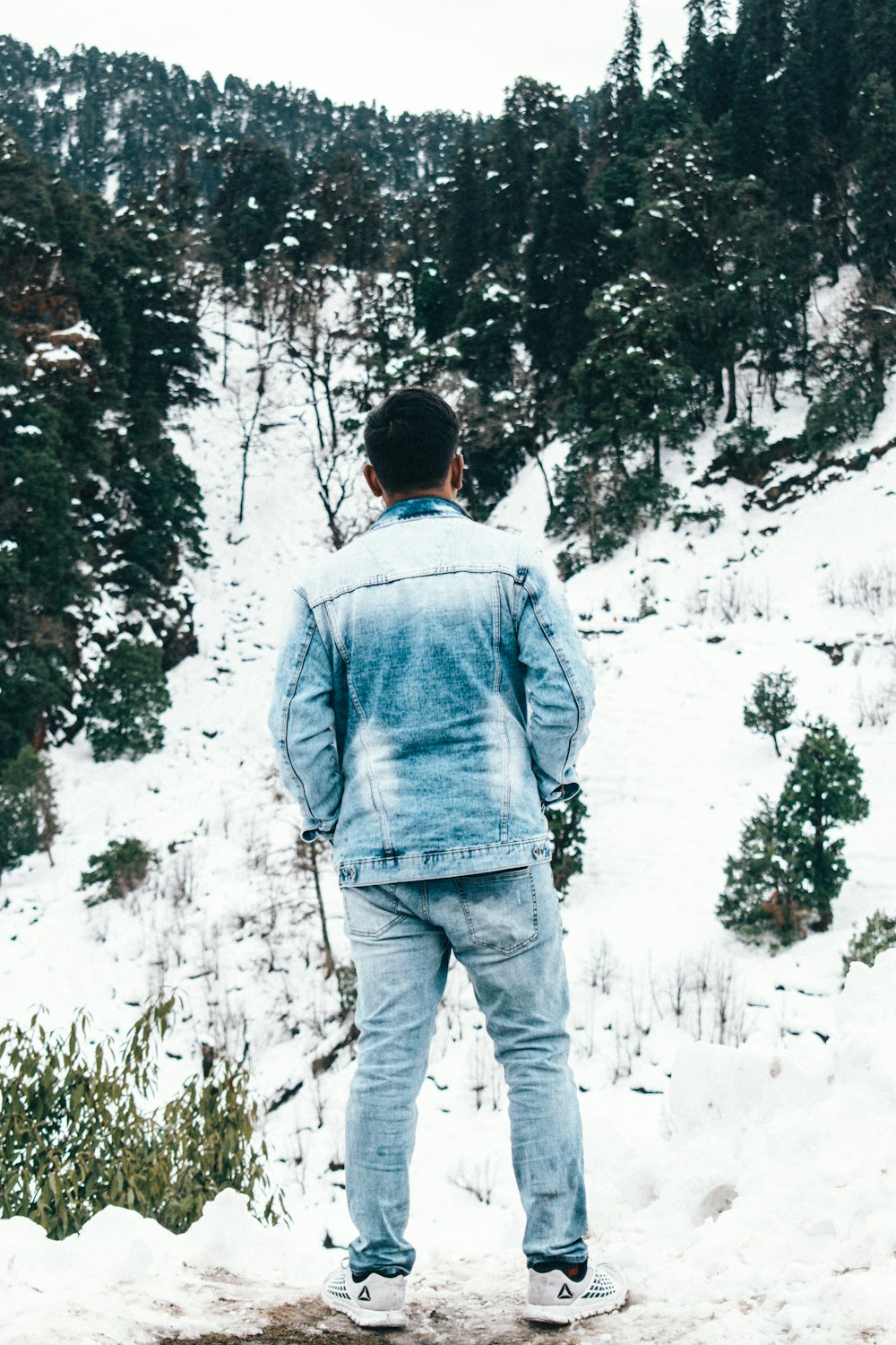 man in blue denim jacket and blue denim jeans standing on snow covered ground