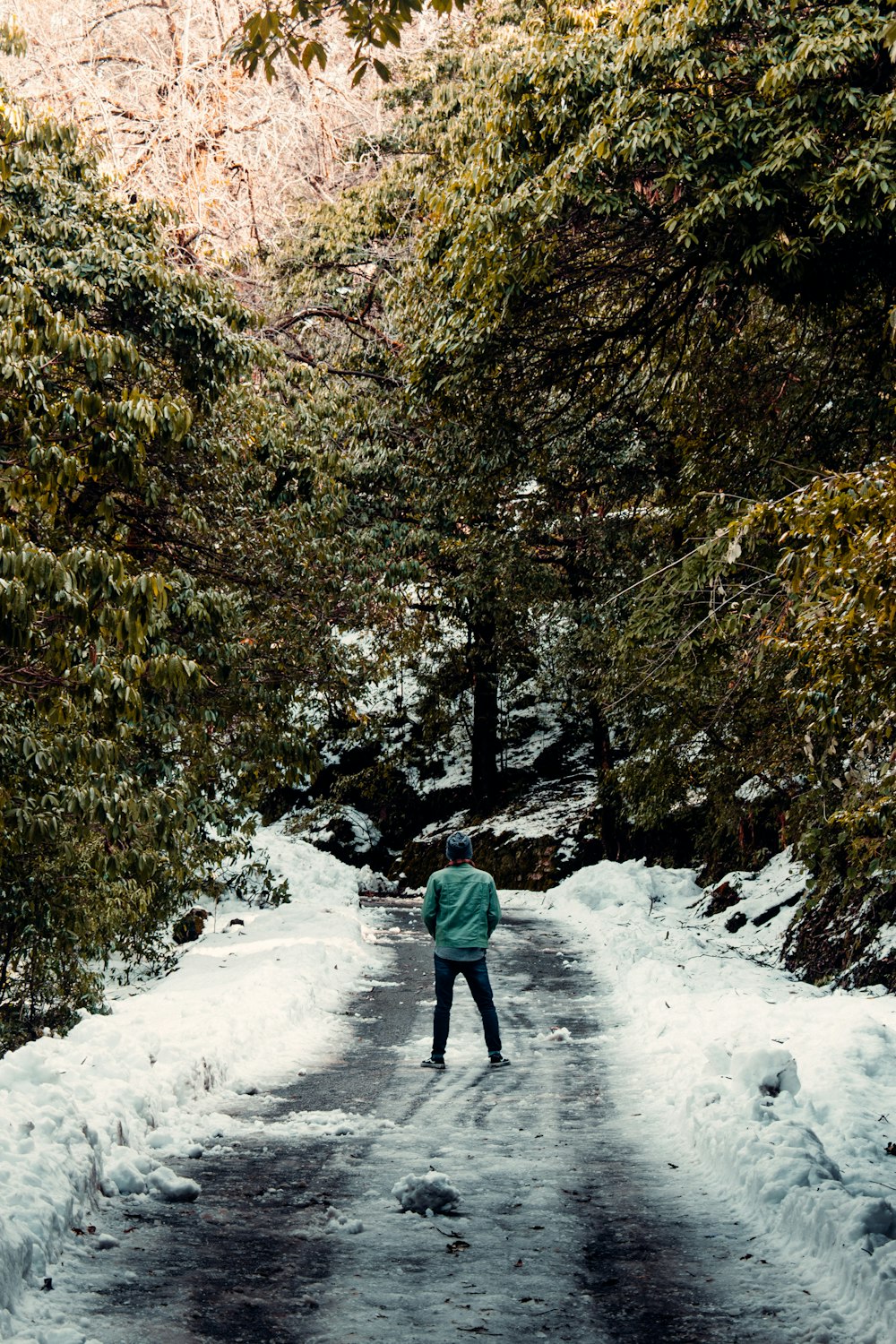 person in green jacket walking on snow covered pathway