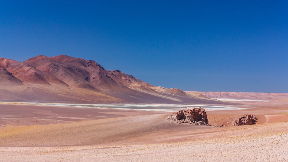 brown sand field near brown mountain under blue sky during daytime