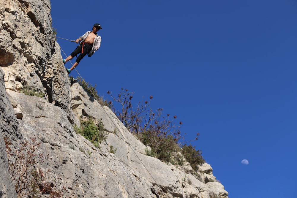homem na jaqueta azul escalando na montanha rochosa durante o dia