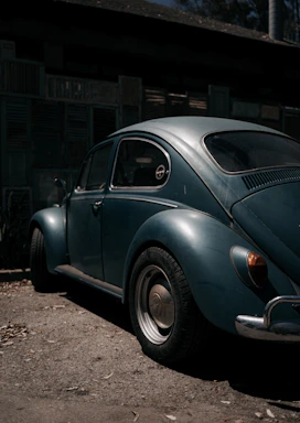 A vintage Volkswagen Beetle parked beside a rustic wooden fence under a clear blue sky.