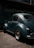 A happy middle-aged man standing proudly beside his restored vintage 1974 Volkswagen Beetle under soft natural light.