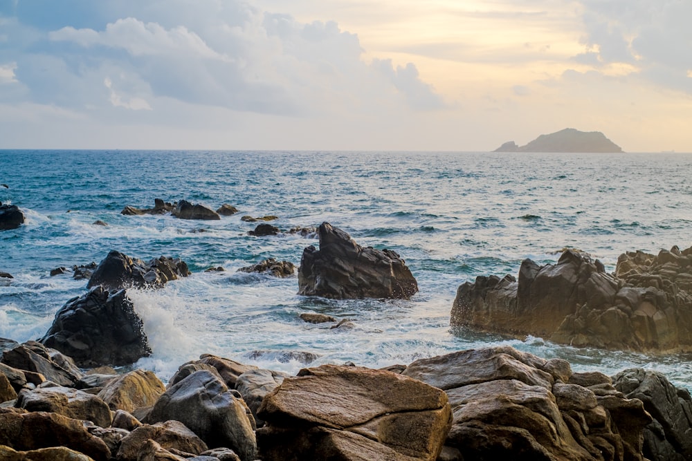 rocky shore with ocean waves under white clouds during daytime