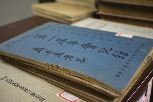 A stack of vintage books with Asian language text on the covers is seen, with the top book featuring a blue cover. The books are slightly worn, suggesting they might be old or well-used.