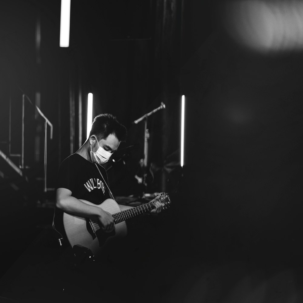 man playing guitar in grayscale photography