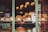 A window display of a bakery featuring various baked goods including croissants and other pastries arranged in wicker baskets. Price tags for each type of pastry are visible. The background shows a warmly lit interior with hanging lights, adding a cozy ambiance.