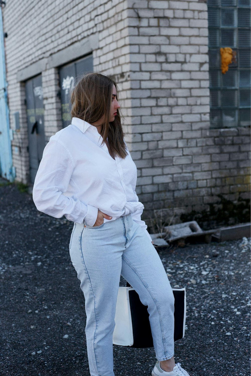 woman in white long sleeve shirt and blue denim jeans standing near brick wall during daytime