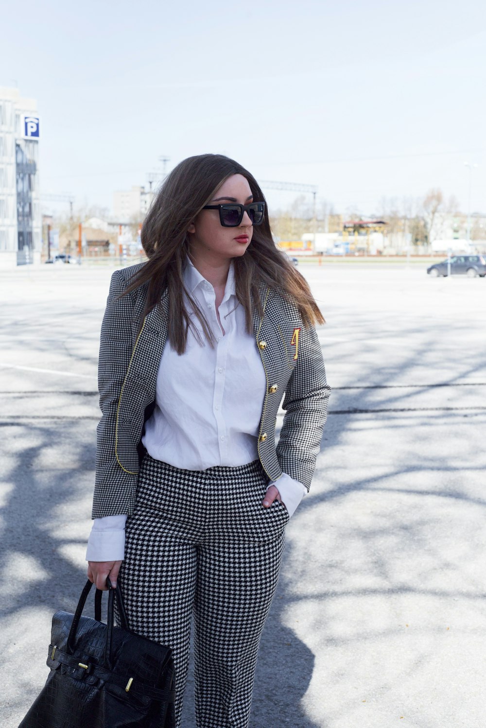 woman in black and white checkered blazer wearing black sunglasses standing on gray concrete floor during
