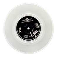 A clear vinyl record with a black label in the center, displaying the text 'Life Begins At The Hop' by XTC, produced by Steve Lillywhite. The label features the Virgin logo and various technical details about the record.