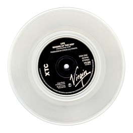 A clear vinyl record with a black label in the center, displaying the text 'Life Begins At The Hop' by XTC, produced by Steve Lillywhite. The label features the Virgin logo and various technical details about the record.