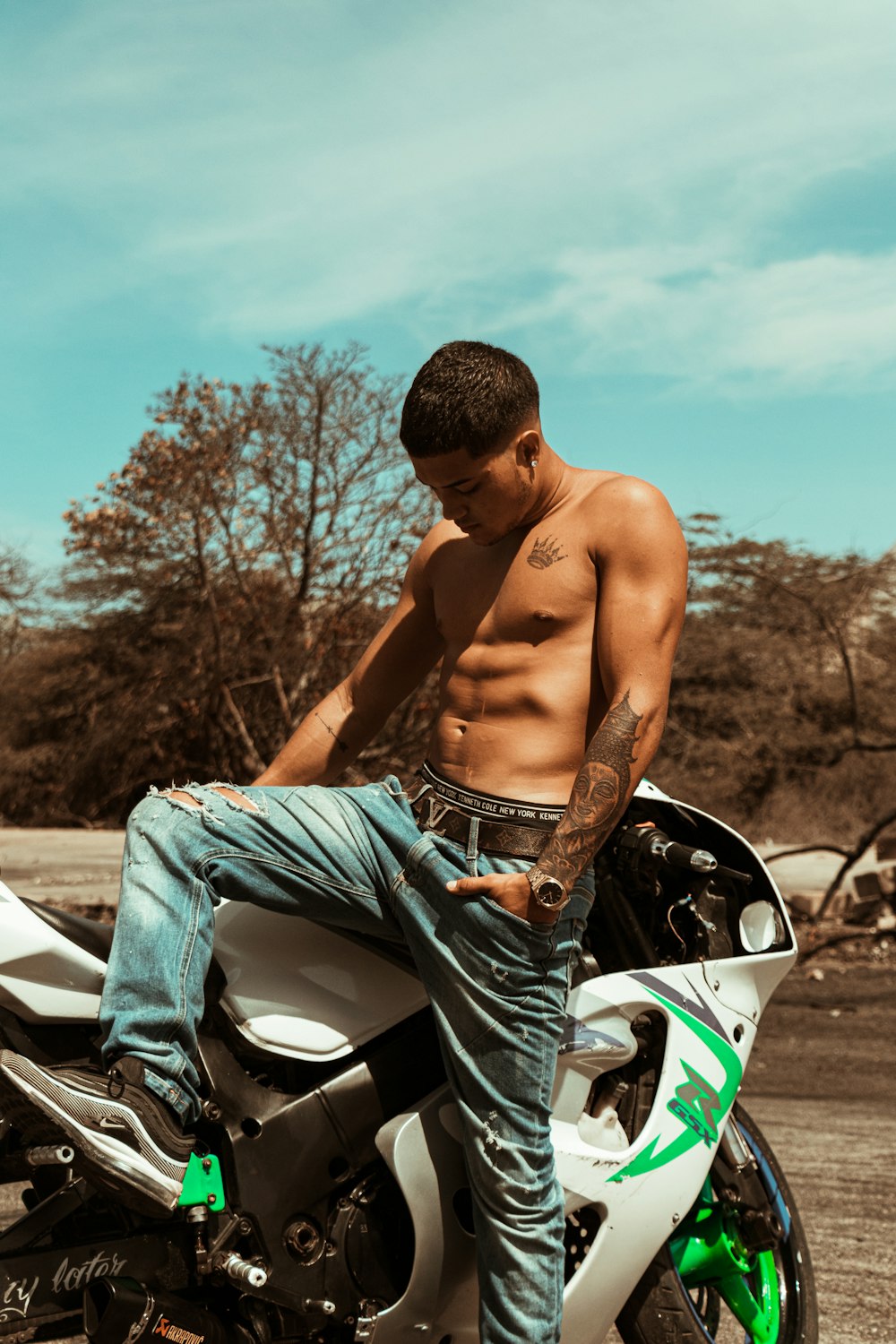 topless man in blue denim jeans sitting on white car during daytime