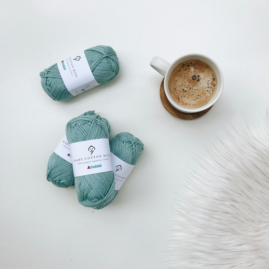 white ceramic mug with coffee beside green yarn