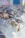 A close-up view of several oysters resting on a bed of ice. The ice cubes are irregular in shape and predominantly translucent, with the oysters displaying rough, textured shells in shades of brown, white, and green. The image has a shallow depth of field, blurring the background.