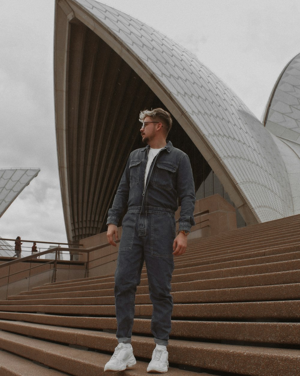 man in blue denim jeans and black leather jacket standing on brown staircase