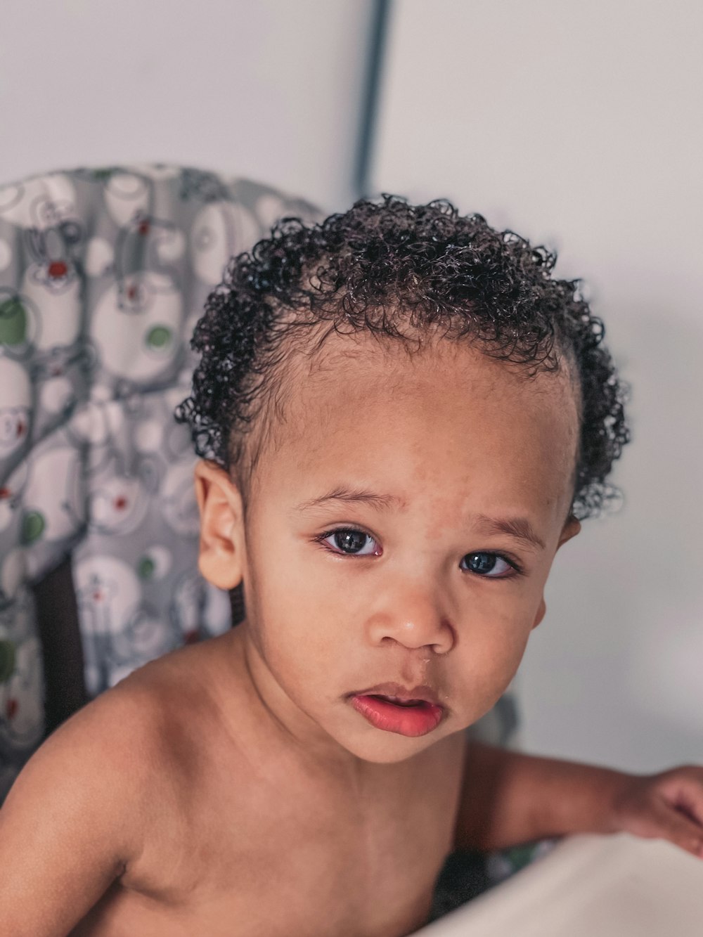 topless boy standing near white and black polka dot curtain