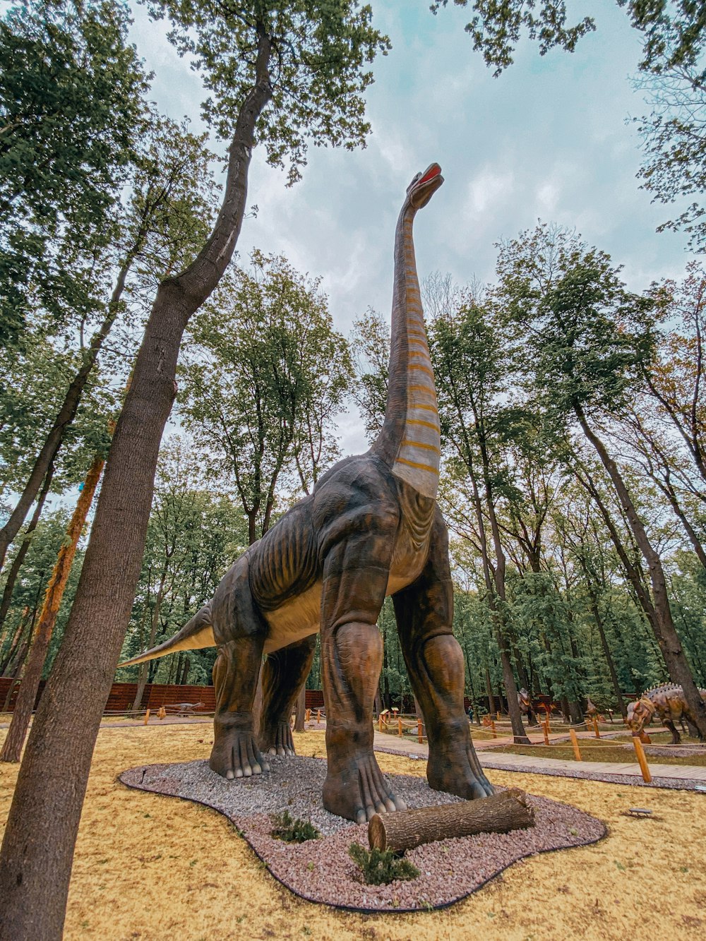brown dinosaur statue near green trees during daytime