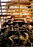 An intricate stone carving of two figures adorns a temple structure. The figures are crafted in a detailed and stylized manner, reminiscent of traditional Indian temple art. The carving is positioned against a background of the temple's architectural elements, viewed from a low angle, emphasizing the vertical lines and intricate design.