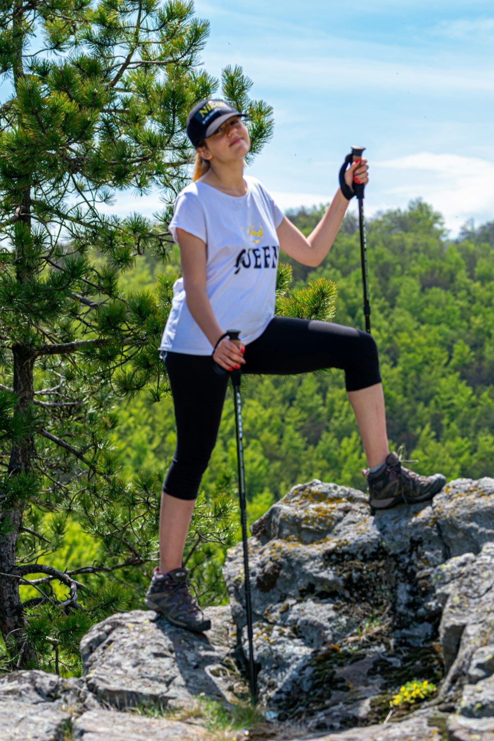 woman in white t-shirt and black pants holding black stick standing on gray rock during