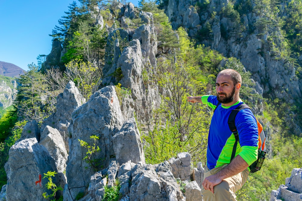 man in blue and yellow long sleeve shirt standing on gray rock during daytime