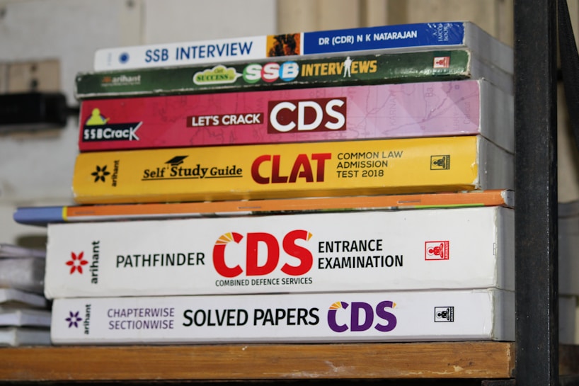 A stack of academic books focused on entrance exams such as SSB Interviews, CDS, and CLAT. The books are neatly arranged, displaying a variety of colors and fonts, each with distinct covers indicating the title and the publisher.