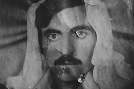 Close-up of a faded, creased photograph being digitally restored on a computer screen.