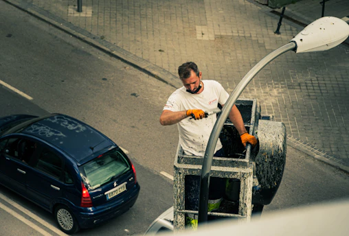 Technicians working on streetlight wiring with fiber optic cables visible nearby at dusk.