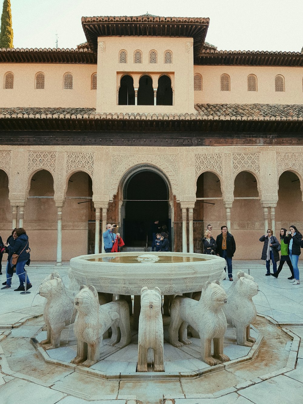 people walking around fountain in front of brown building during daytime