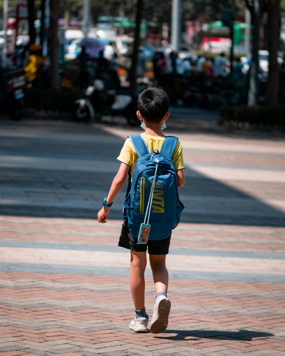 boy in blue and yellow t-shirt walking on sidewalk during daytime