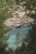 A scenic view featuring clear turquoise waters surrounded by lush green trees and rocky cliffs. In the background, several rustic buildings are nestled among the rugged hillside, providing a sense of seclusion and tranquility.